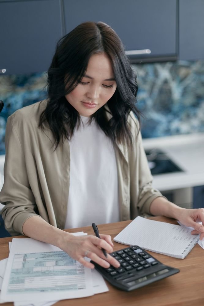 A woman working out figures on a calculator beside paperwork and a notebook