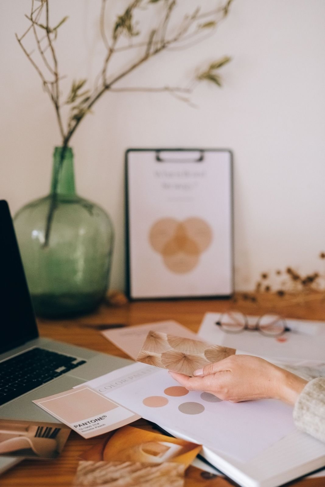 A hand holding a pattern card over a colour palette on a design desk