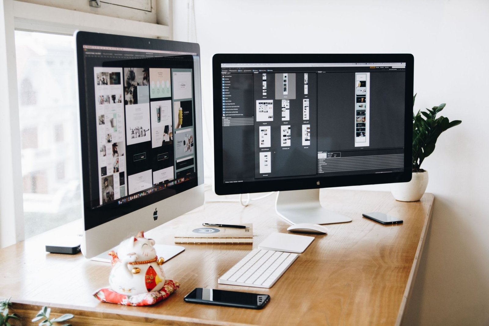 Two desktop screens on a wooden desk showing website designs in progress