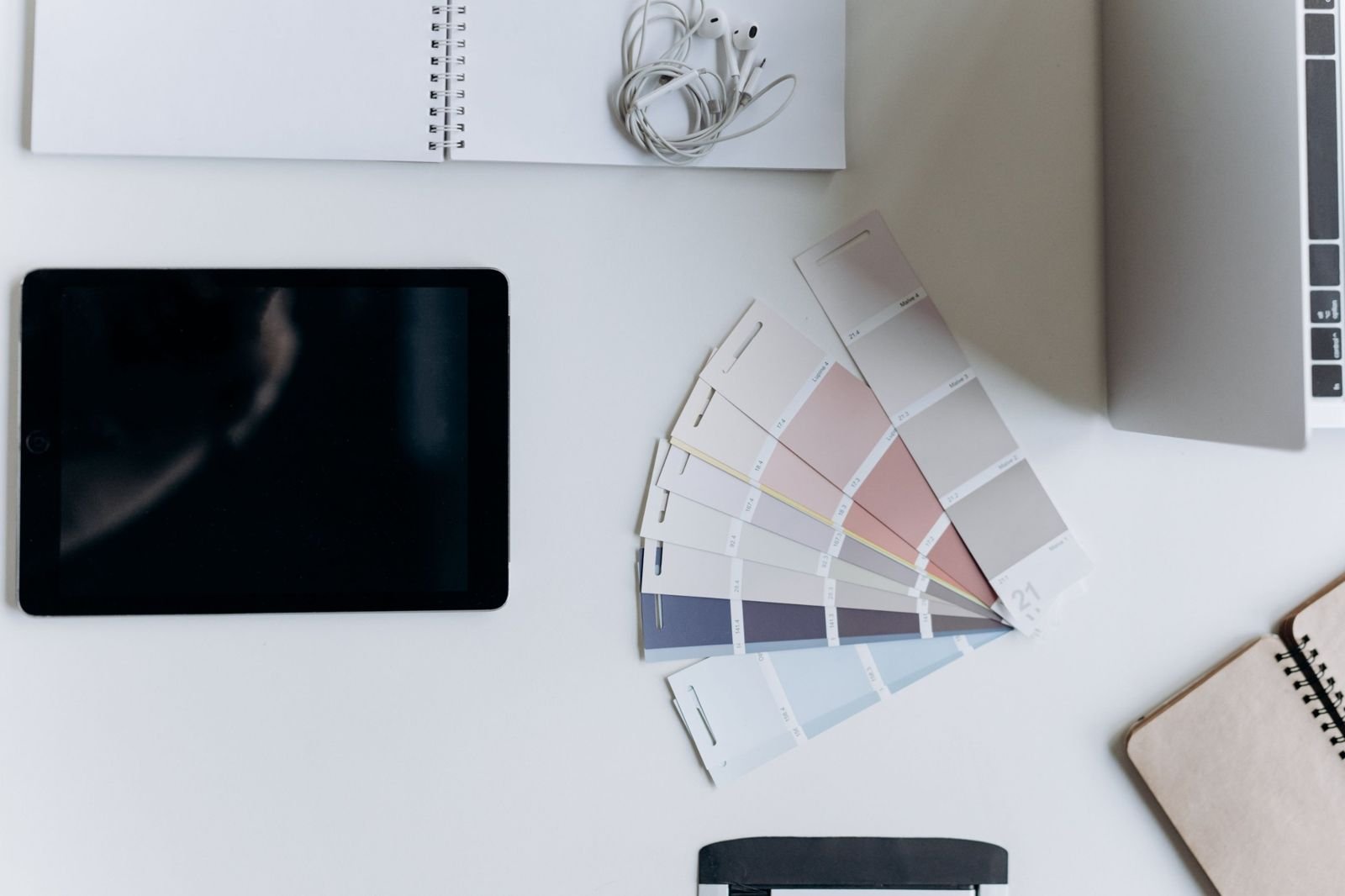 A tablet, notebook and fan of colour swatches laid out on a white desk