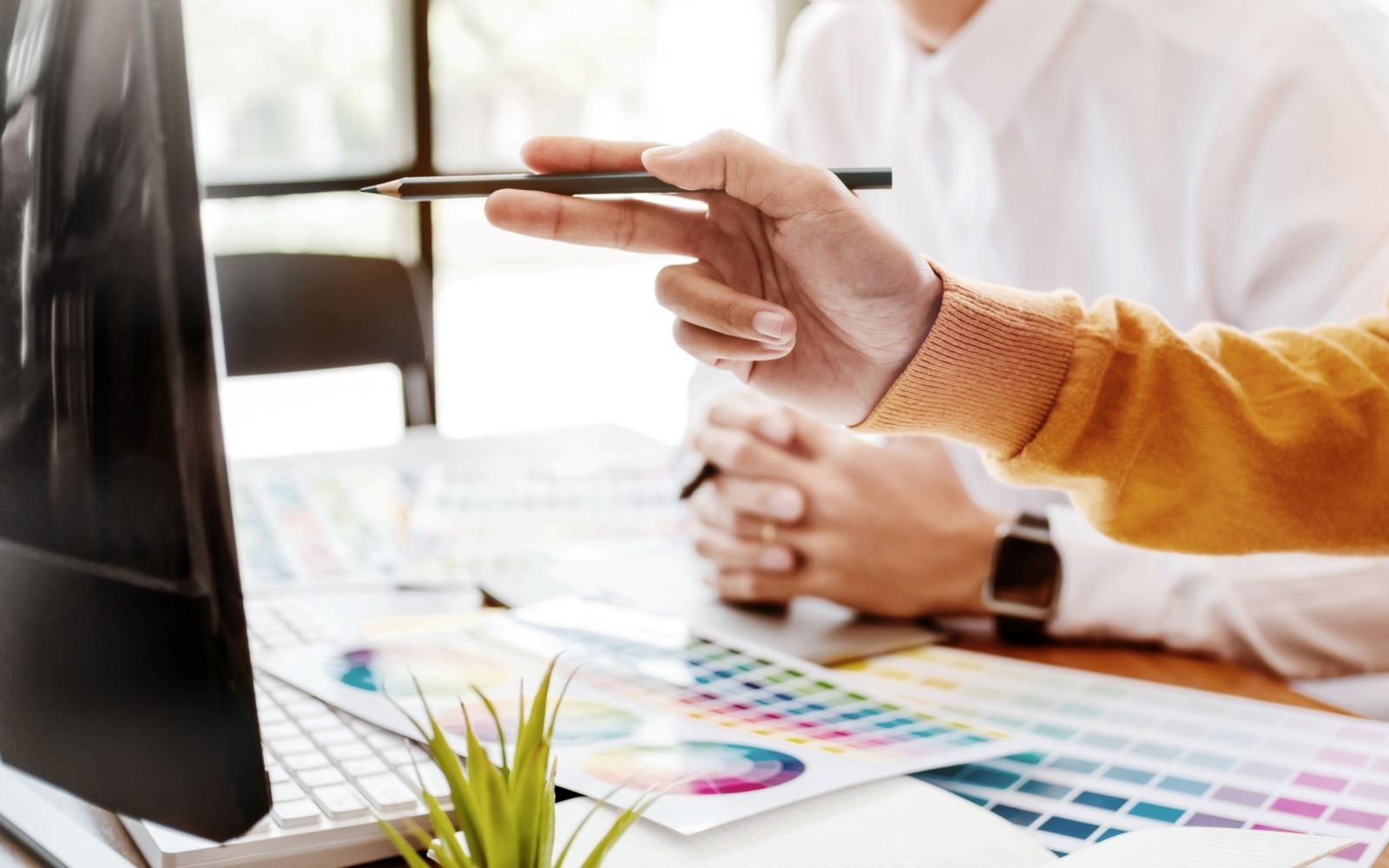 Pointing a pencil at a screen during a design review, with colour swatches spread across the desk