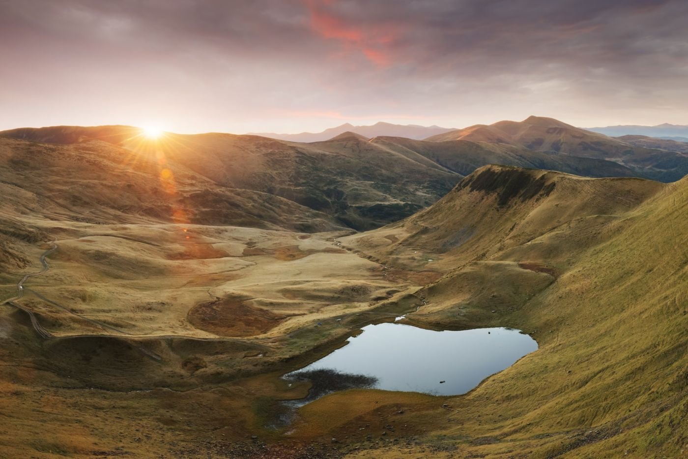 Sunrise over rolling golden hills and a still upland lake