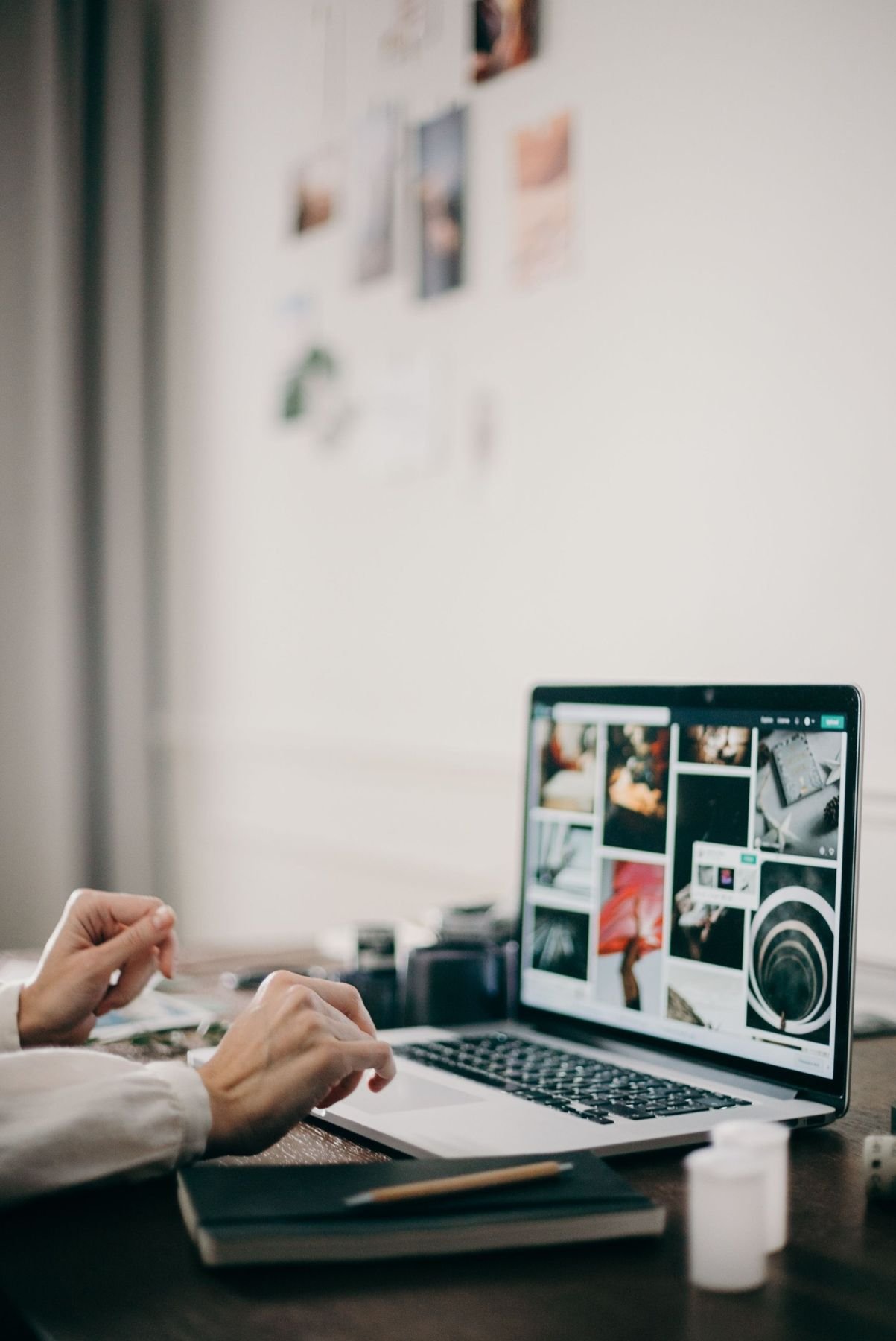 Editing a gallery of photos on a laptop, with prints pinned to the wall behind