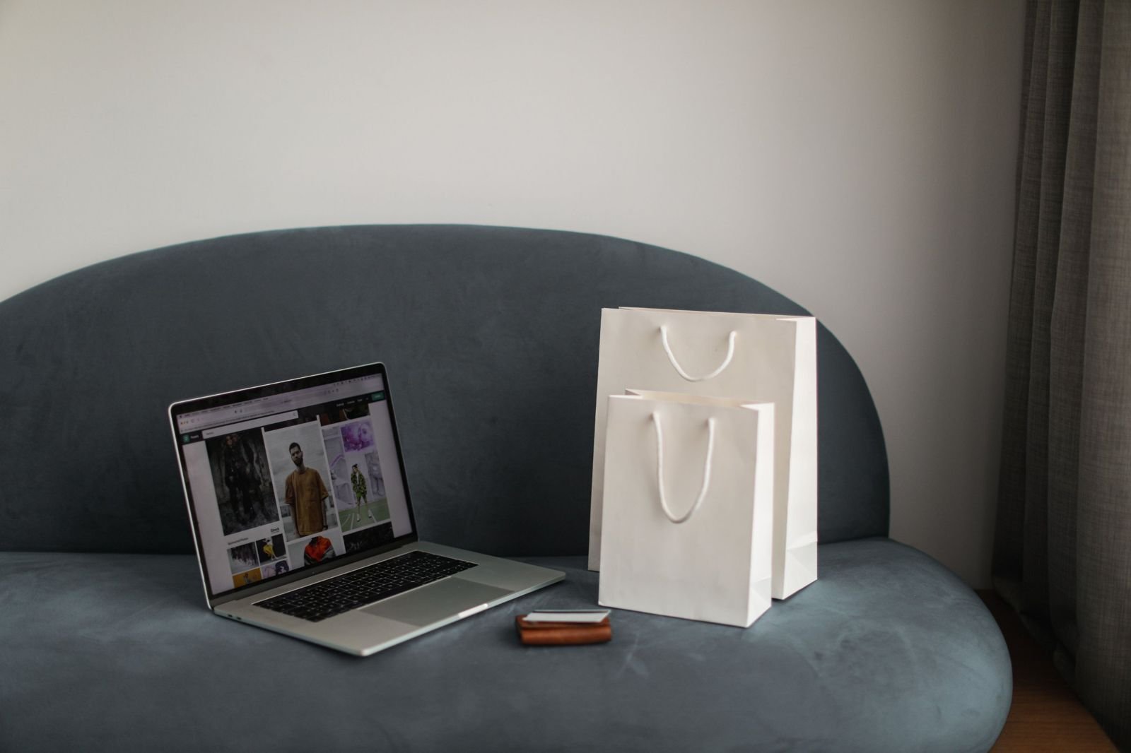 A laptop showing an online shop on a sofa beside two paper shopping bags