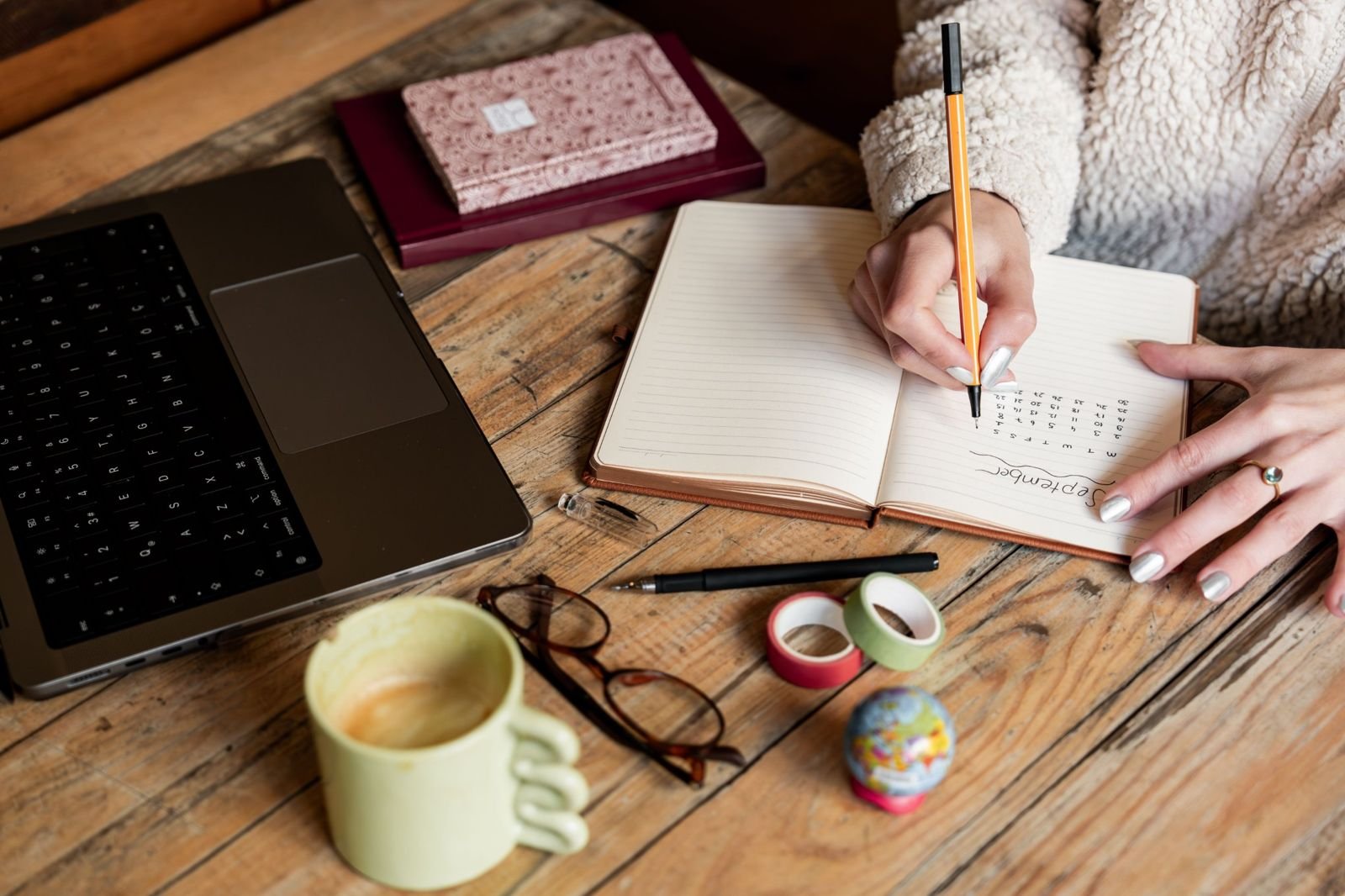 Hands writing a plan in a notebook beside a laptop and coffee mug