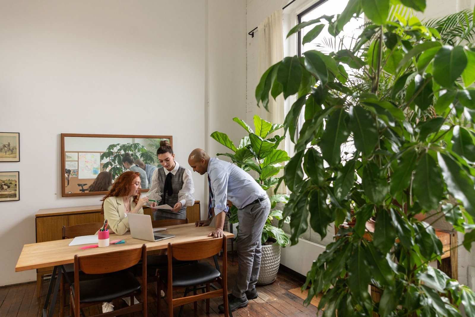Three people talking through a project around a laptop in a bright office full of plants