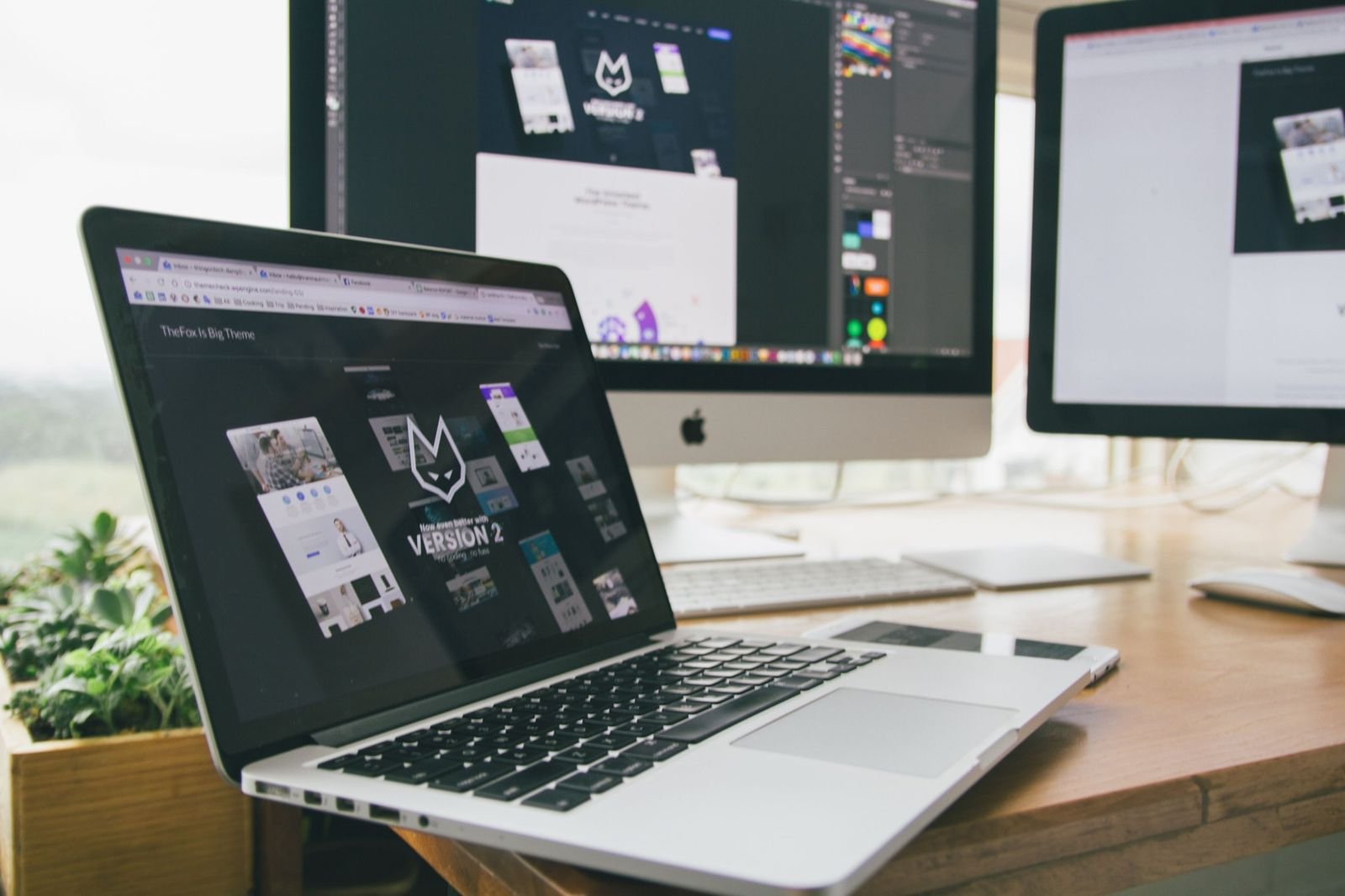 A laptop and two desktop screens showing website designs in progress