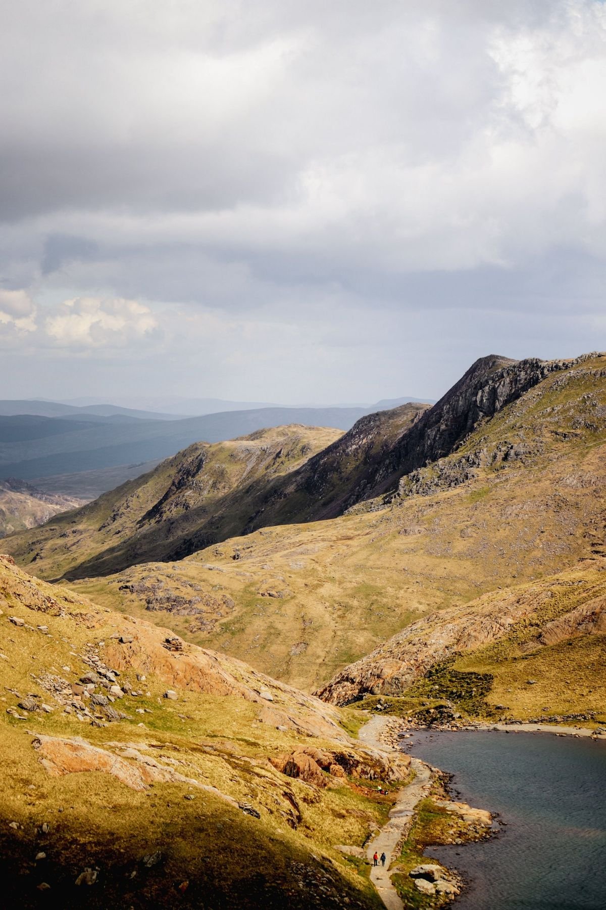 Walkers on a path beside a mountain lake in the Welsh hills