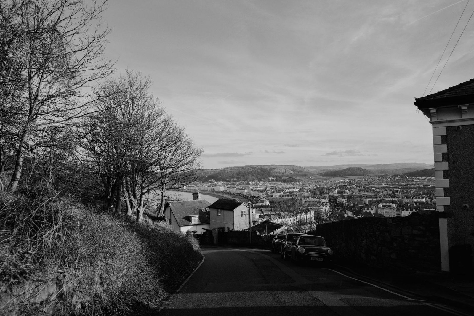 A black and white view down a hill over a Welsh town, with hills beyond